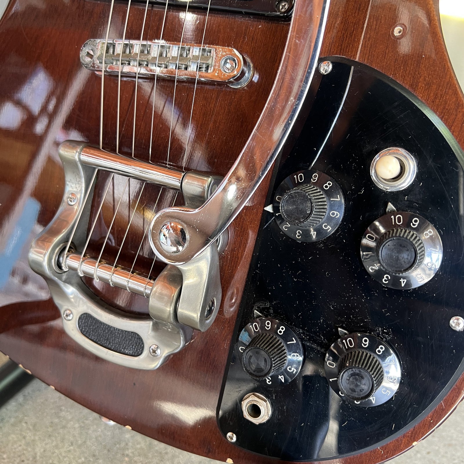 Close-up detail of the Bigsby-style vibrato tailpiece, roller bridge, and black control knobs